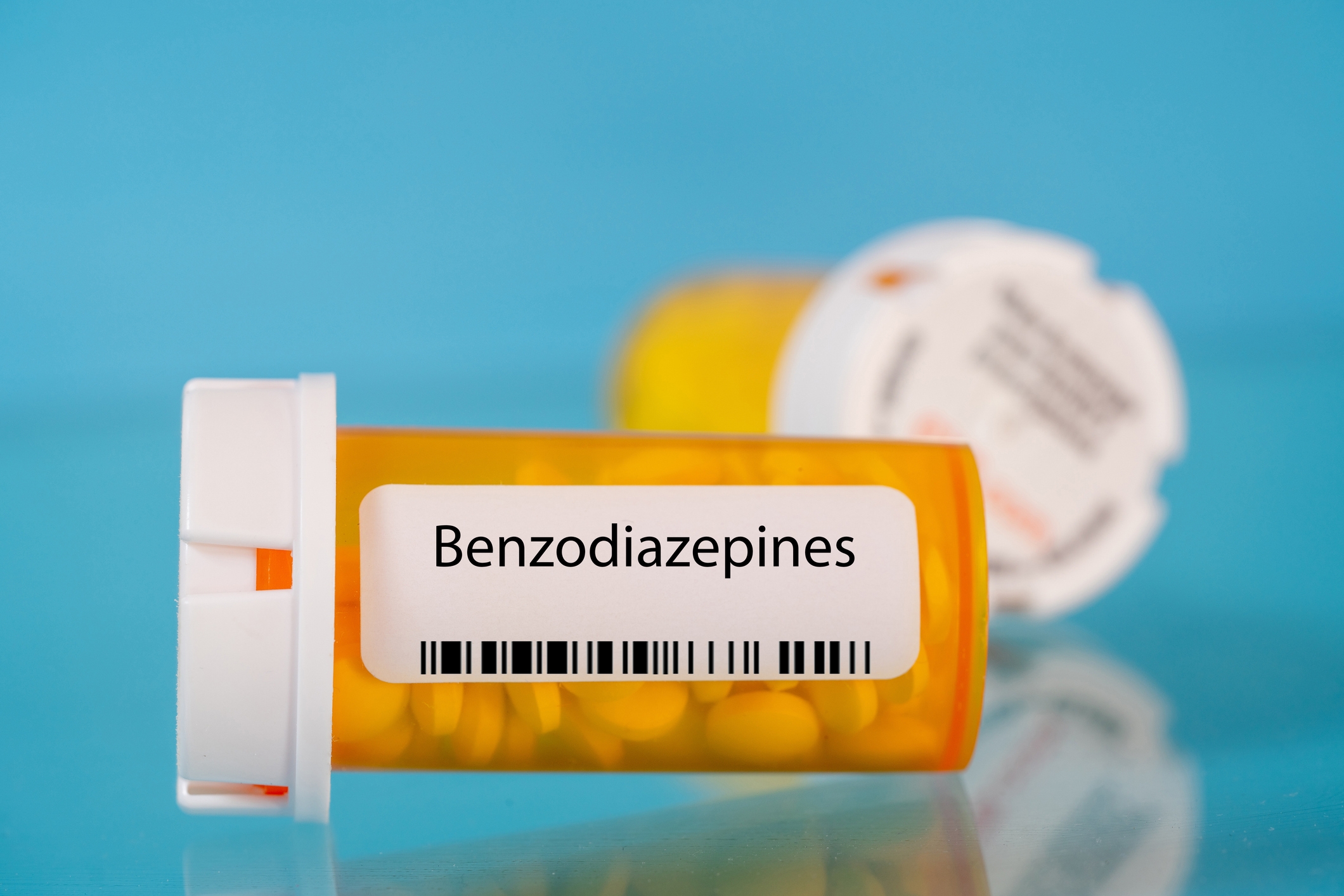 Prescription bottle labeled "Benzodiazepines" against a blue background, with a second, blurred bottle in the background