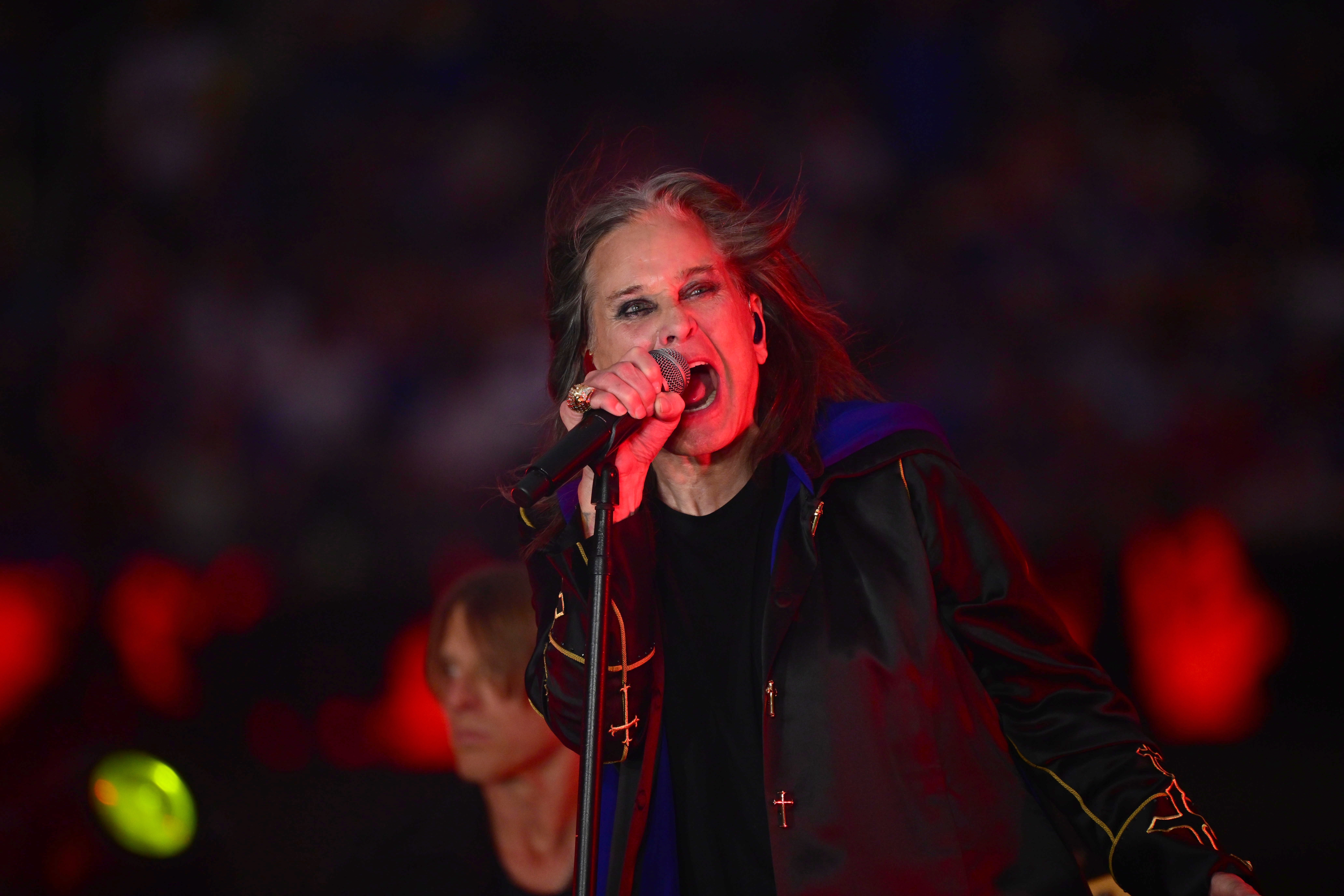 A singer passionately performs on stage, wearing a dark jacket with gold details
