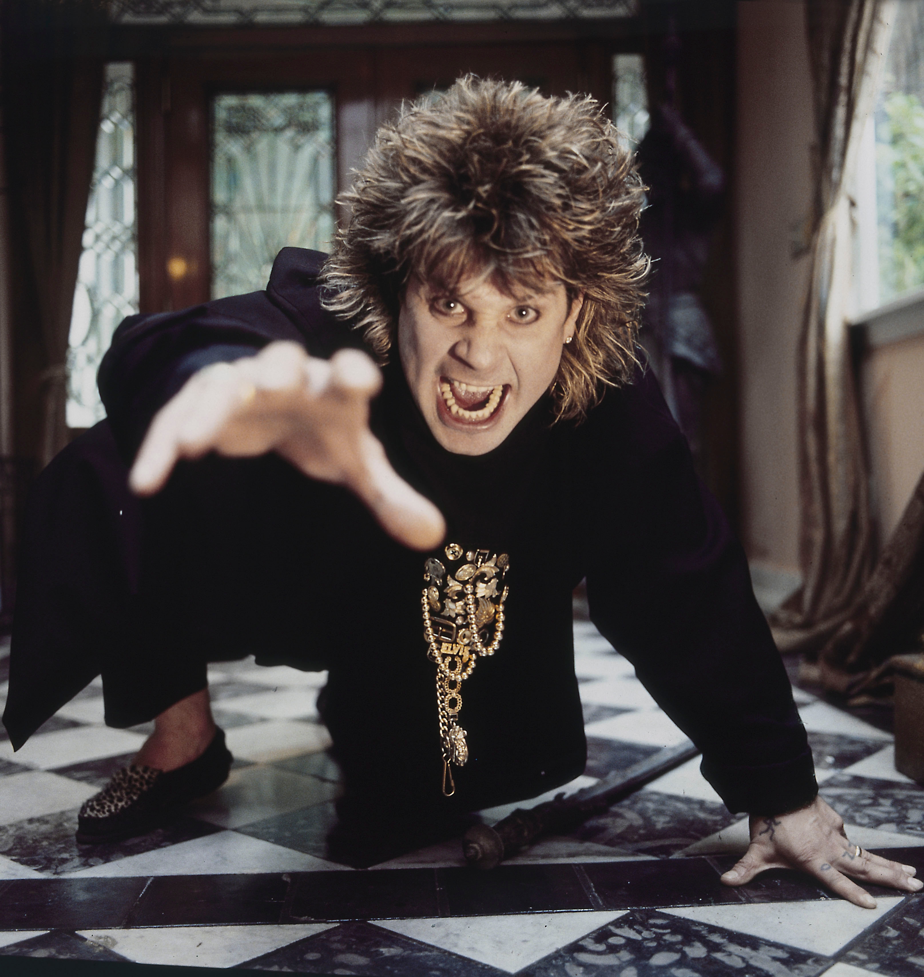 Person in dramatic pose on checkered floor, reaching toward camera, wearing robe-style clothing with ornate chain detail