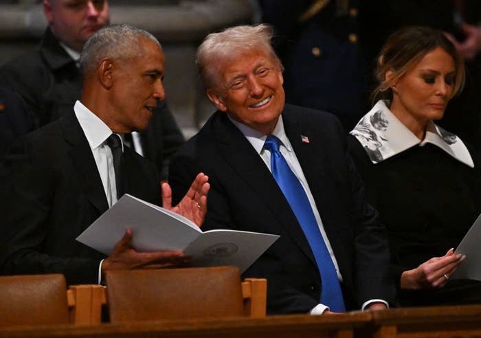 Three people seated at an event, engaged in conversation. One man holds a program, another smiles broadly. A woman sits beside them, looking down