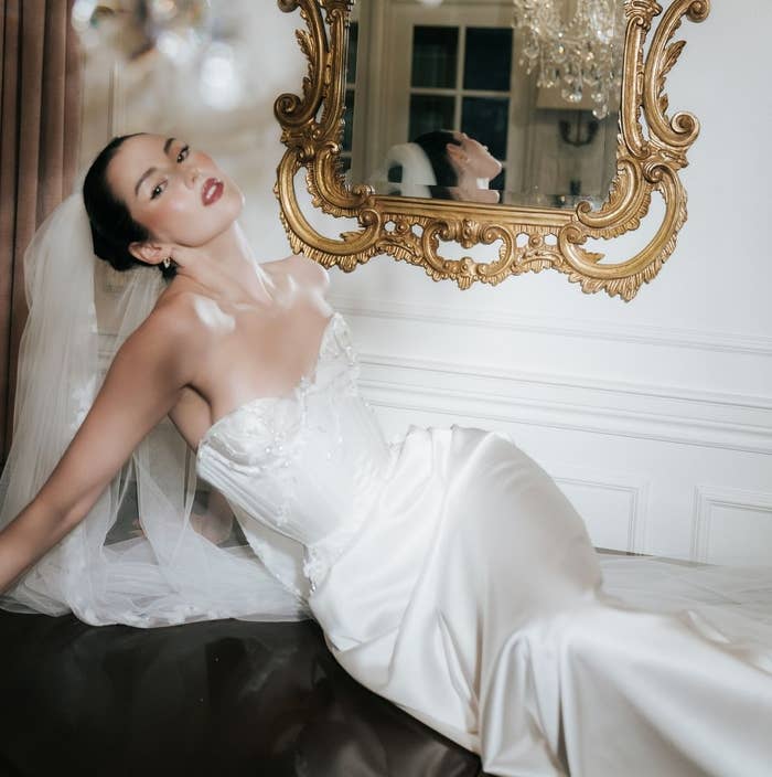 Persona en vestido de novia elegante y velo, recostada en un sofá frente a un espejo ornamentado