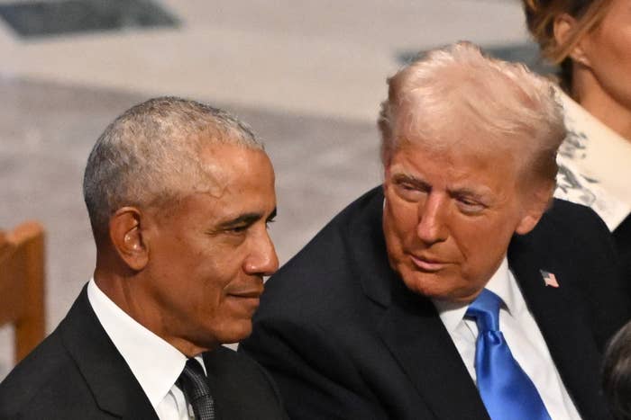 Two men in suits sitting next to each other at an event, engaged in conversation