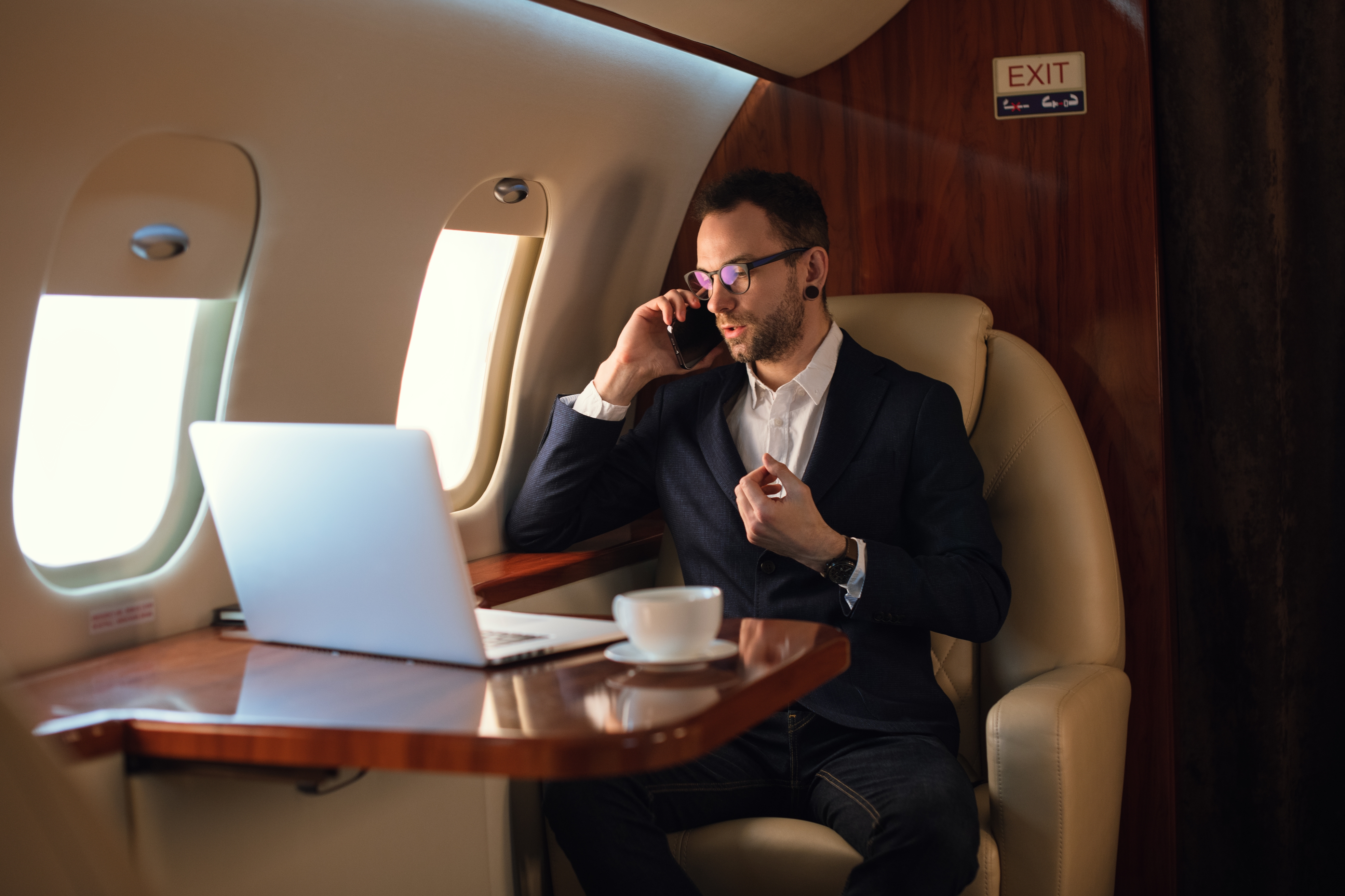 Man in suit using laptop and phone on private jet