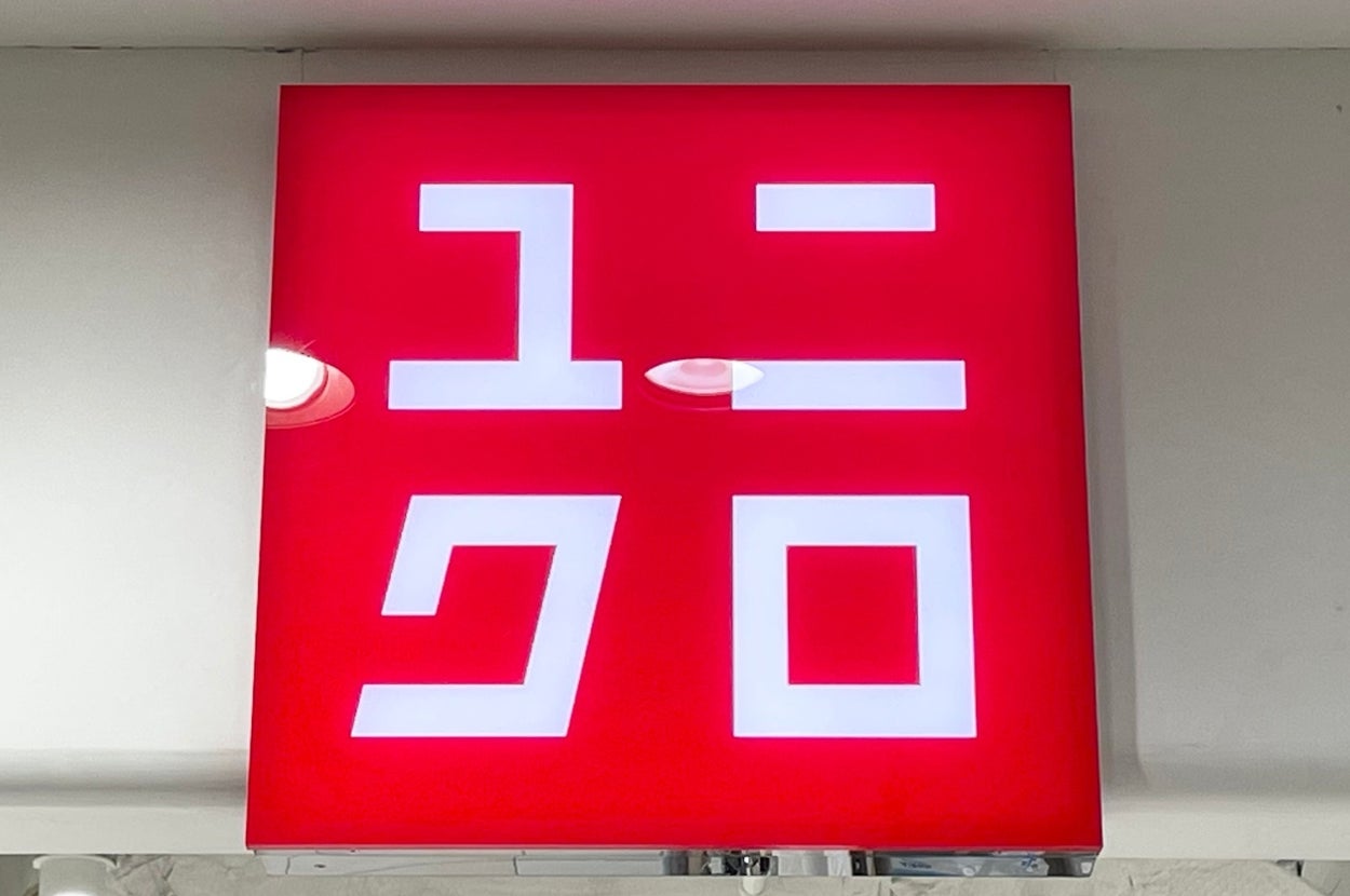 A red sign with white Japanese katakana characters, spelling out a brand name, hangs above a store entrance