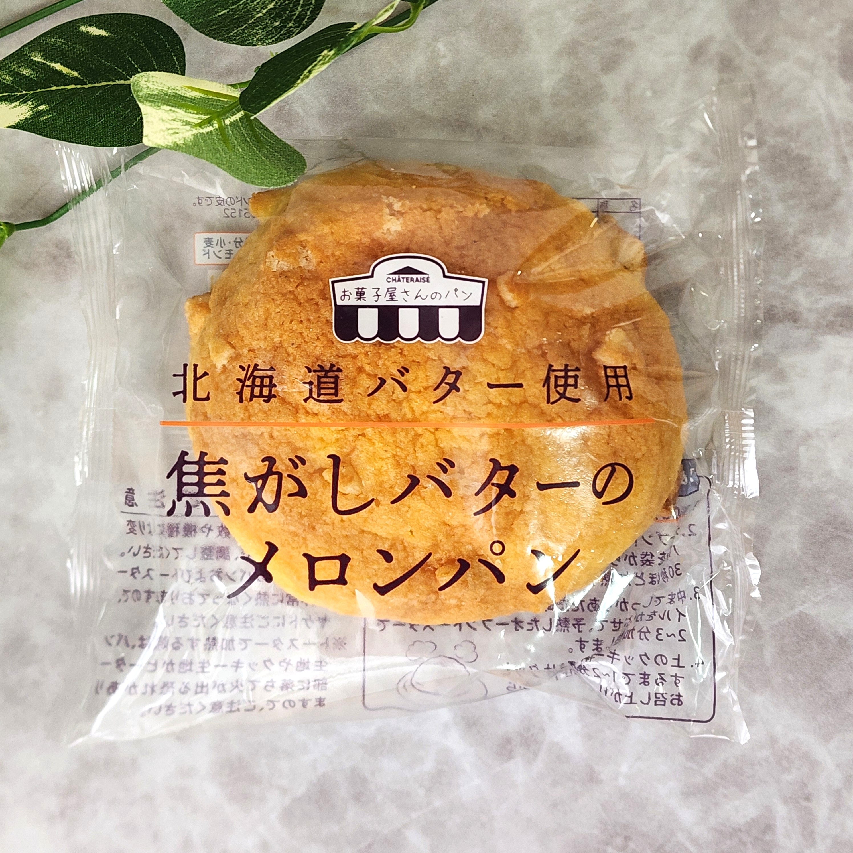 北海道バター使用の焦がしバターのメロンパンが透明な袋に包まれている。背景に葉が少し見える。