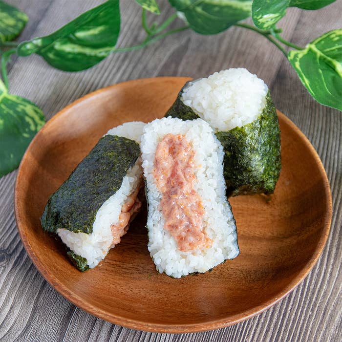 おにぎり3個が木の皿に盛られ、葉が飾られた背景で撮影されています。一つは中身が見えています。