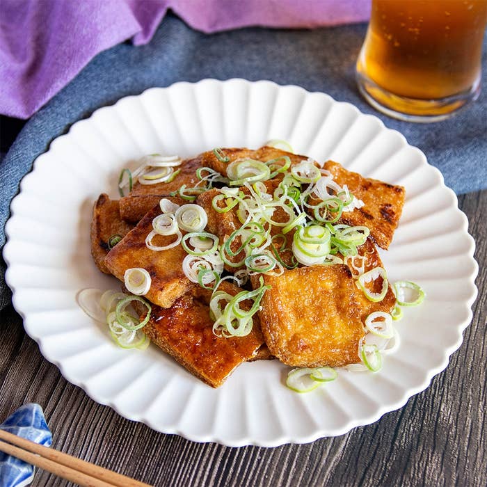 皿の上にねぎがのった油揚げ料理。添えられた飲み物が見える。