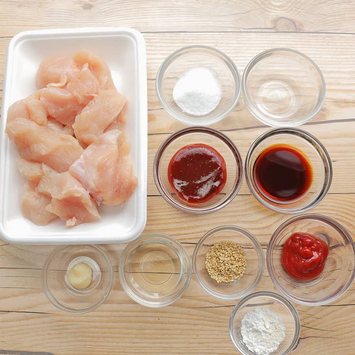 調理用の鶏肉と調味料が並んだ料理の準備シーン。小皿にはソースや調味料が入っています。