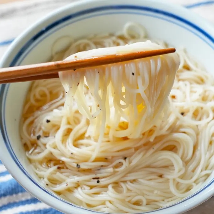 箸で持ち上げられたそうめんが入った器。シンプルな料理の紹介。