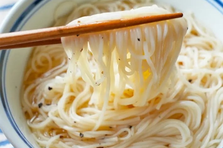 箸で持ち上げられたそうめんが入った器。シンプルな料理の紹介。