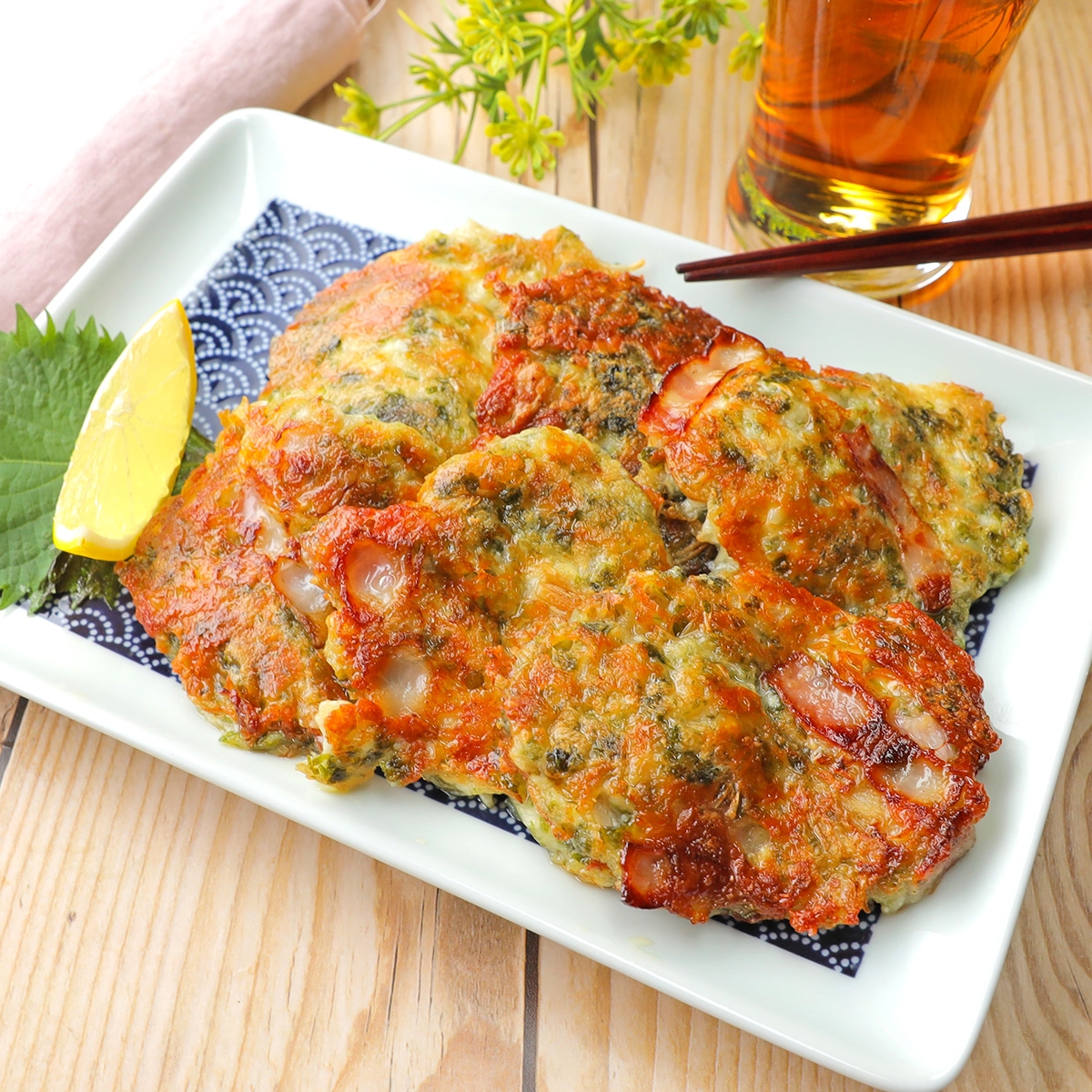 和風の具だくさんかき揚げが白い皿に盛られている。横にレモン、飲み物も添えられている。