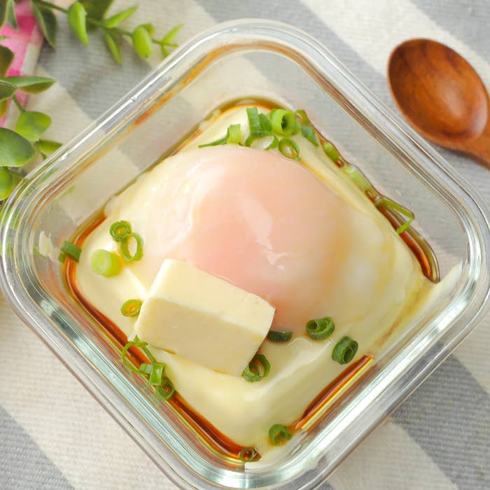 温泉卵と豆腐が入ったガラスの器。上には刻みネギと醤油がかかっている。横に木のスプーンと植物が添えられている。