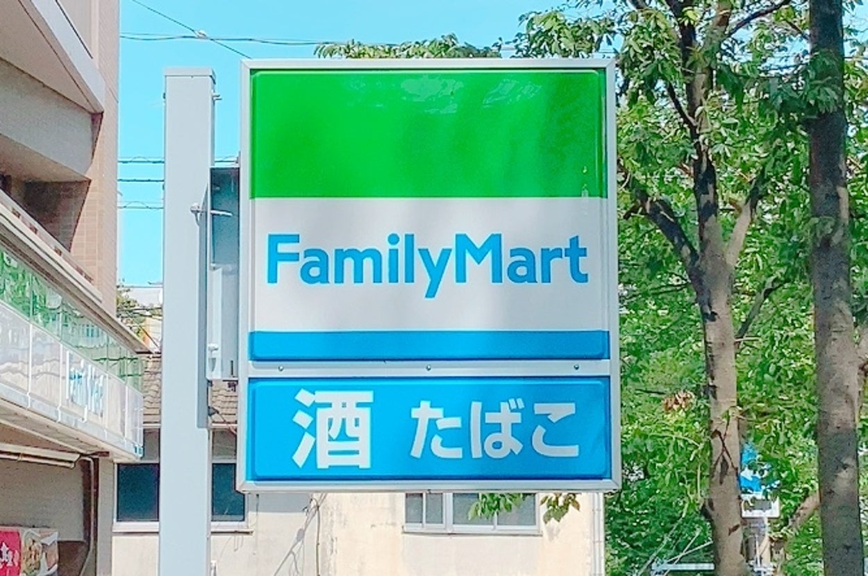 ファミリーマートの看板。酒やたばこを販売していることを示す表示が見える。周囲に緑の木々が立ち並ぶ。