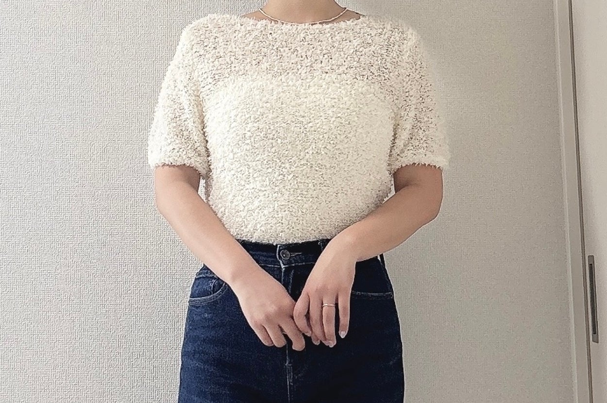 女性がシンプルなトップスとジーンズを着用し、カジュアルな雰囲気で立っています。