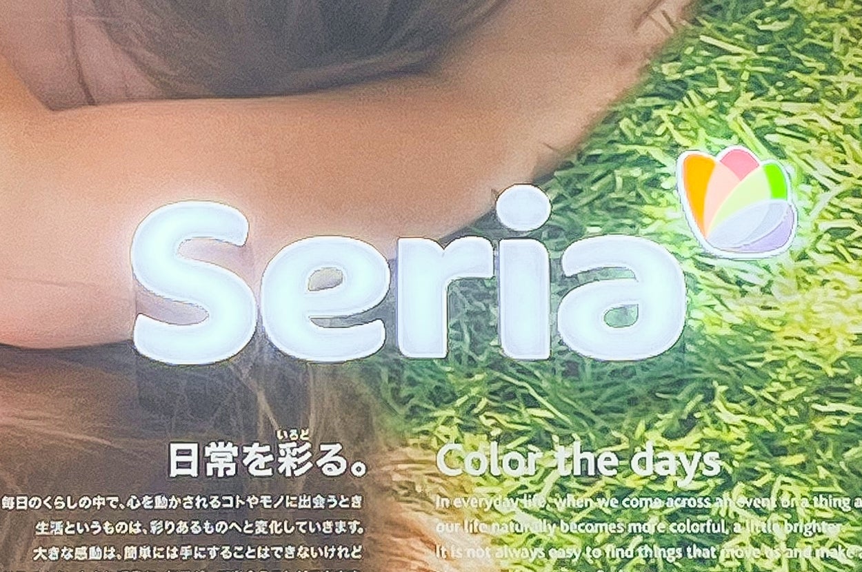 Seriaの広告。日常を彩るというキャッチフレーズ。「Color the days」と書かれ、芝生の上に横たわる女性の姿が一部見える。