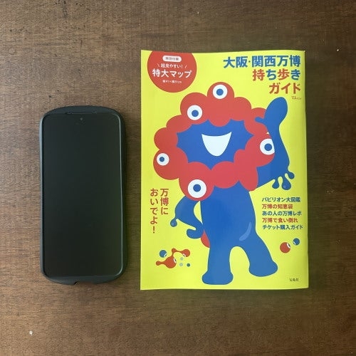 スマートフォンとユニークな赤青キャラクターが印刷されたガイドブックが木製のテーブルに置かれている。
