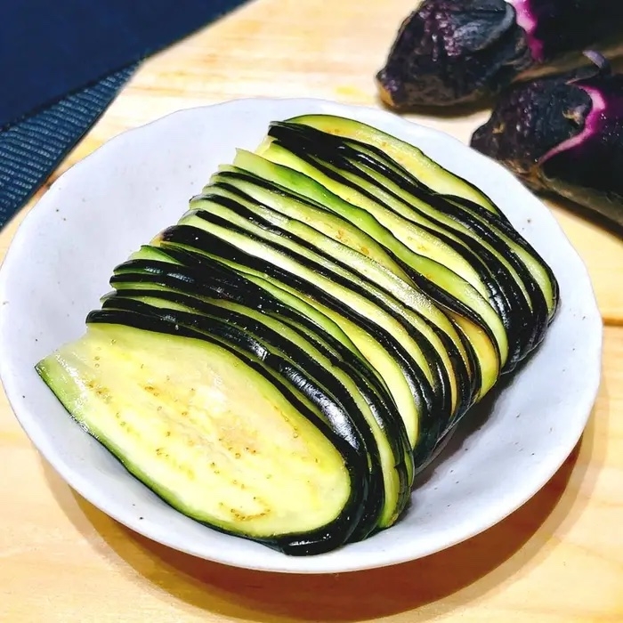 陶器の皿に並べられたスライスされたナス。食材が美しく整然と並べられている。