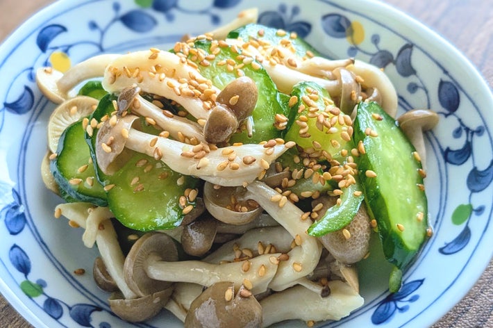 きゅうりとキノコにゴマが振りかけられたサラダが、模様付きの皿に盛られている。