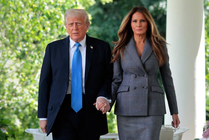 Two people holding hands, walking together outside. The woman is wearing a tailored suit