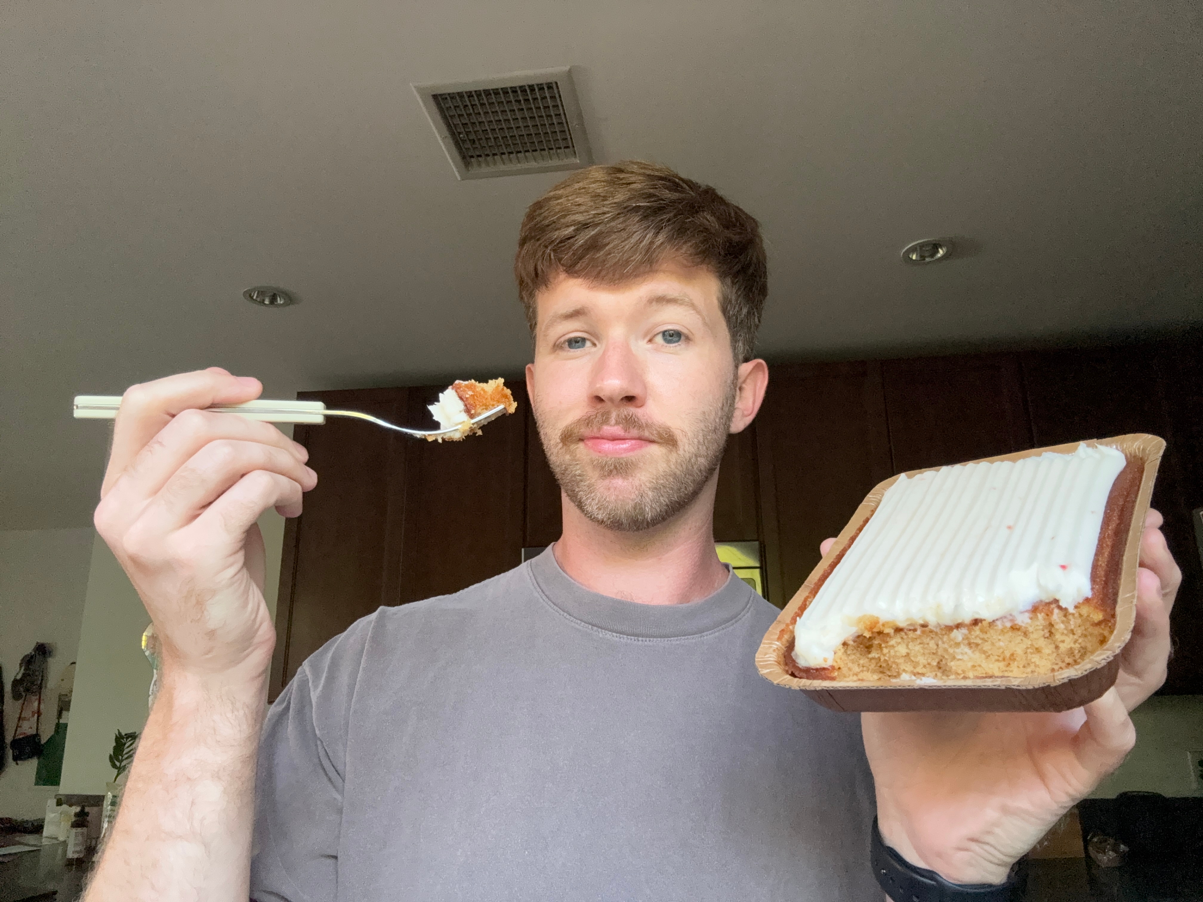 Person holding a fork with cake and a partially eaten rectangular cake with frosting in a kitchen
