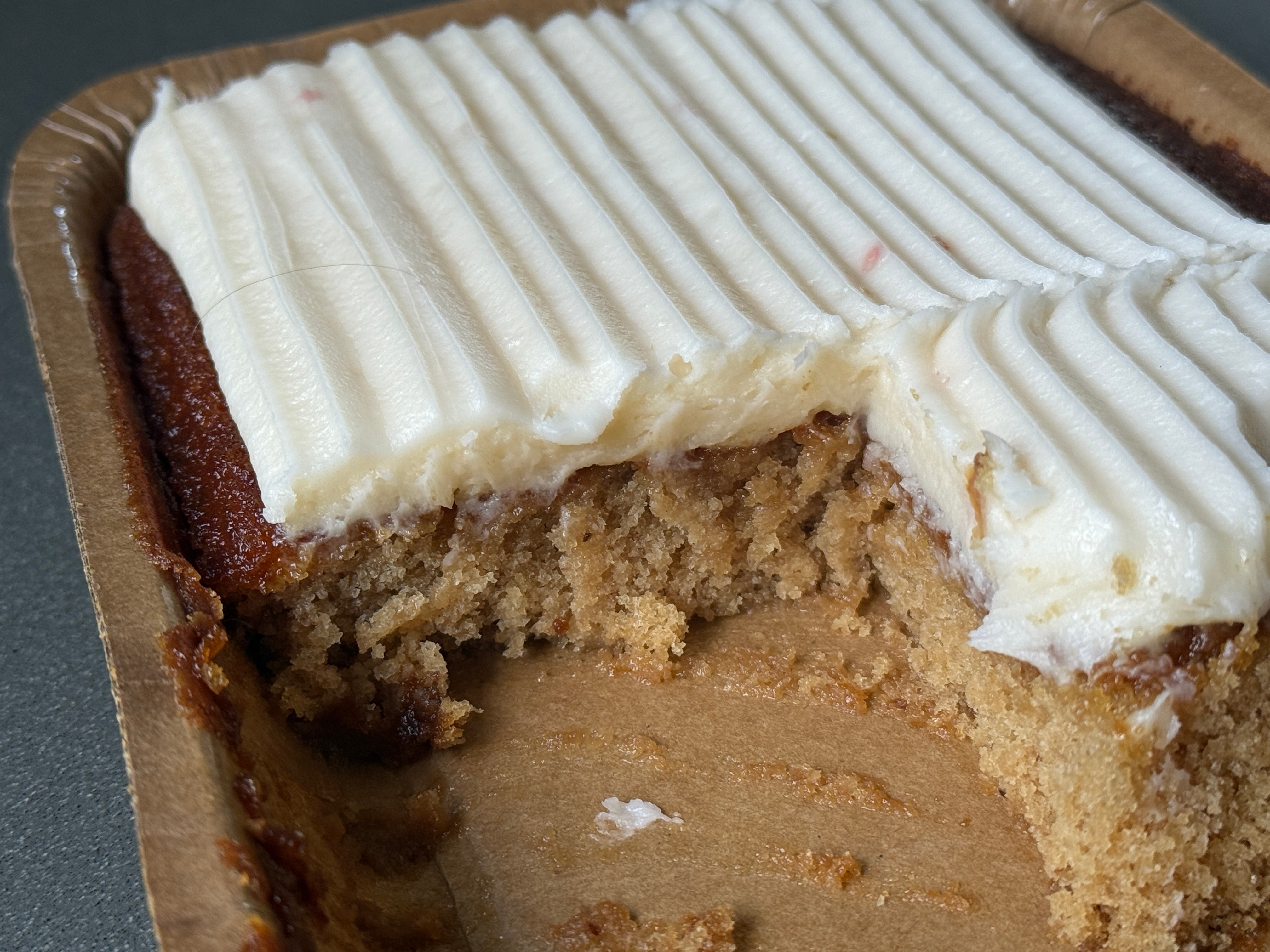 Cake with a missing piece, topped with ribbed white frosting, in a brown container