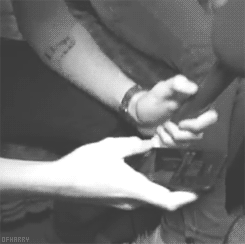 Persona mostrando un teléfono a otra persona sentada, que tiene un tatuaje visible en el brazo