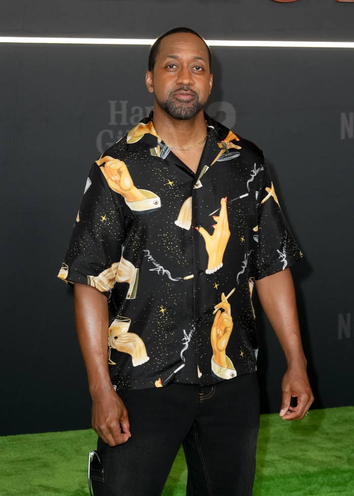 Jaleel White poses on the red carpet wearing a patterned shirt with artistic hand designs and pants