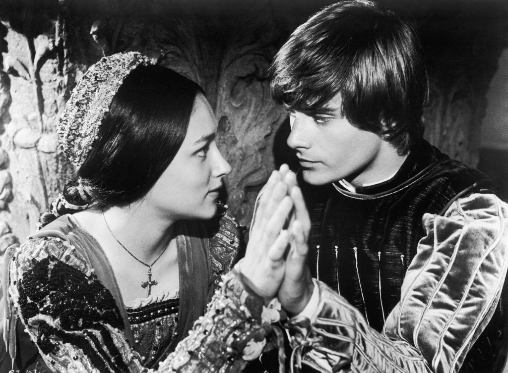 Two people in period costumes face each other, touching palms. They appear serious and focused on each other