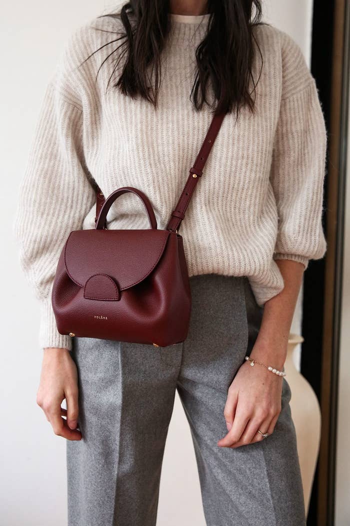 Persona con suéter de punto y pantalones de vestir, lleva un bolso de mano al hombro