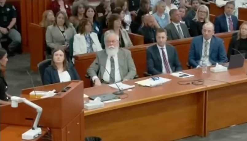Courtroom scene with a legal team seated at a table, facing a judge's bench, amidst several people in the audience
