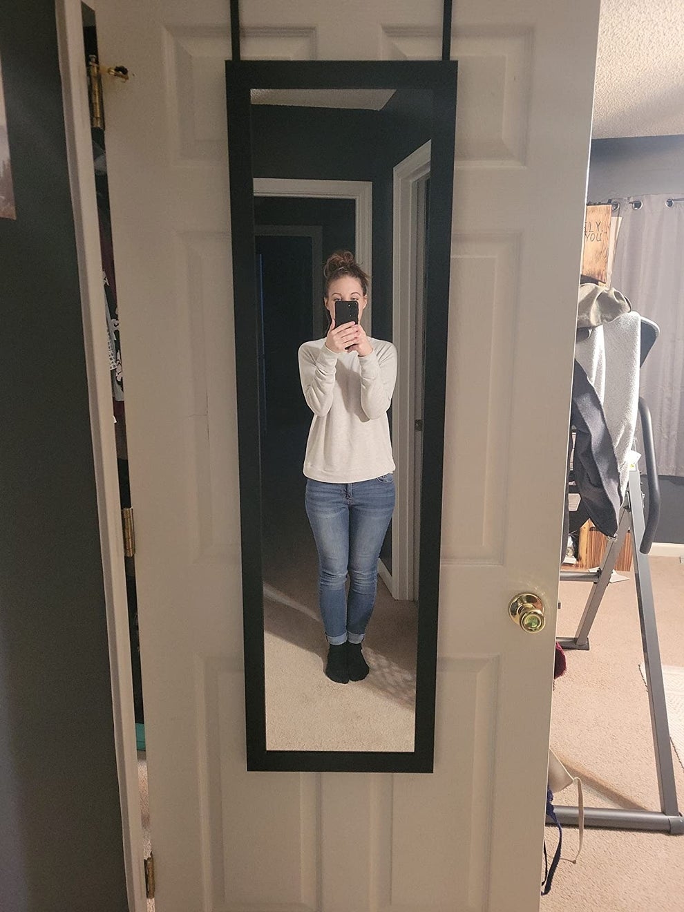 Person taking a mirror selfie in casual clothes, including a light sweater and jeans, in a home setting