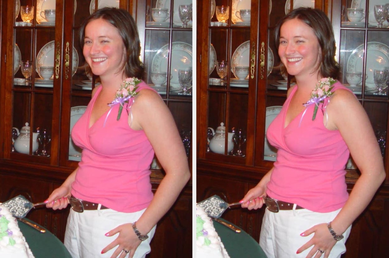 Person smiling, wearing a pink top with floral accents and white pants, holding a cake server in front of a wooden display cabinet with dishes