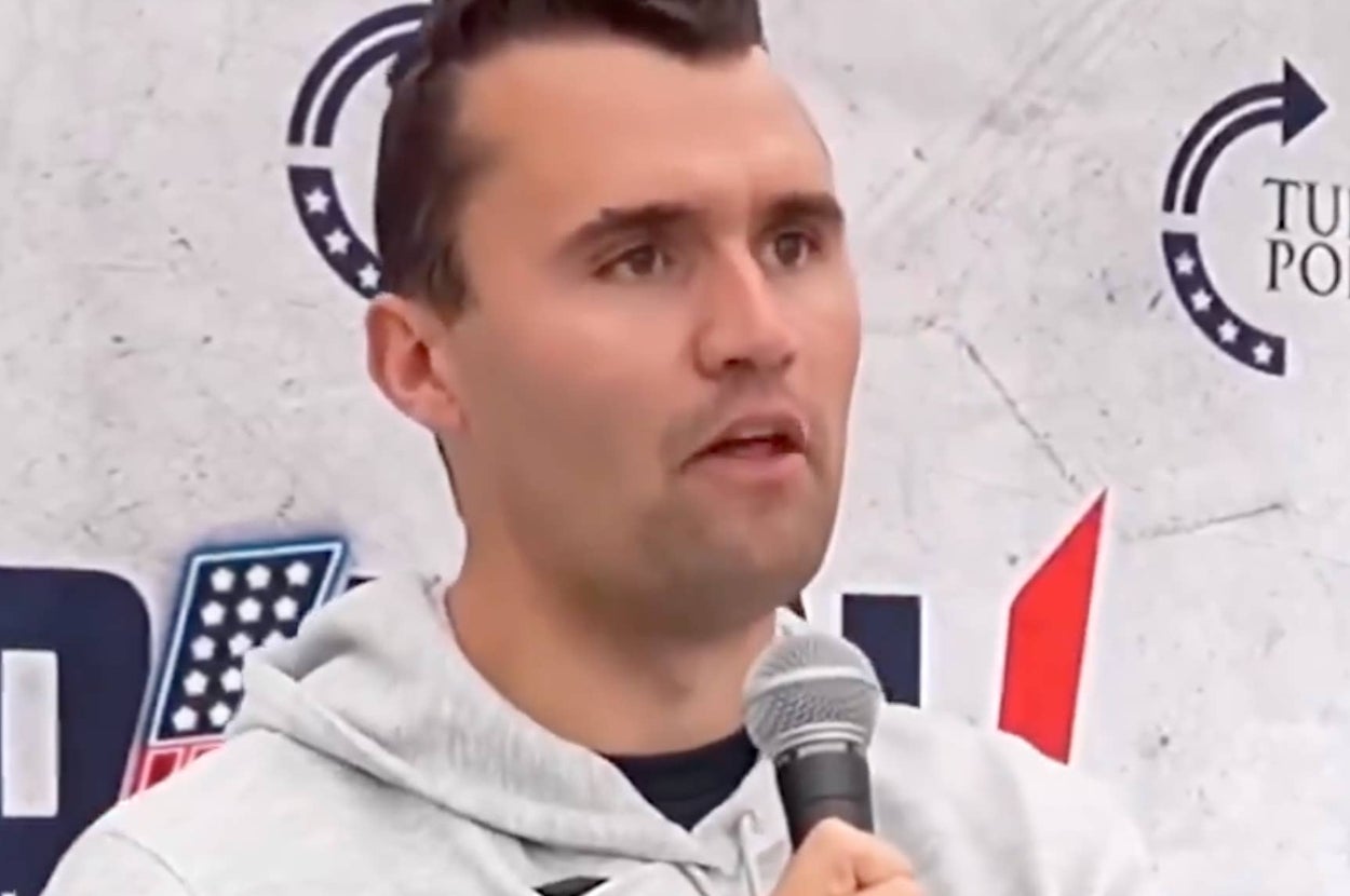 Person speaking into a microphone at an event with logo backdrop
