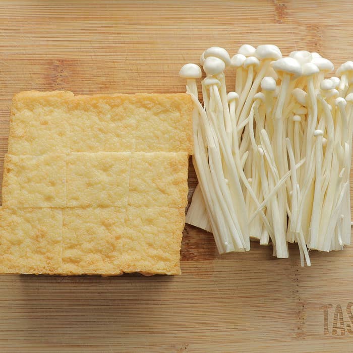 えのき茸と四角い揚げ豆腐が木製のまな板の上に並んでいる。