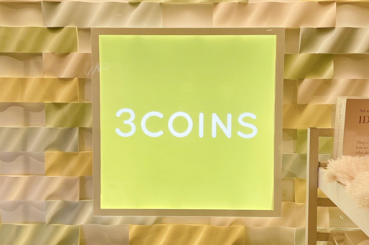 「3COINS」の看板が壁に掛かっています。背景は立体的なデザインです。