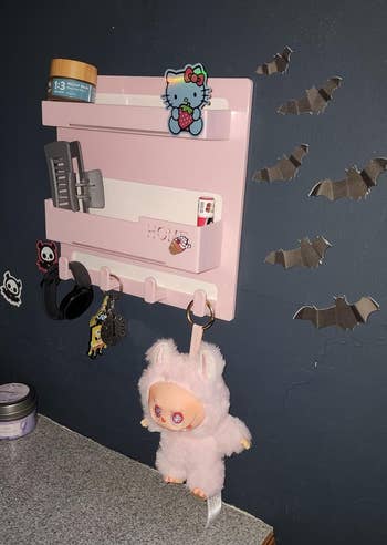 Wall-mounted organizer with Hello Kitty decor, hanging plush toy, grooming products, and bats connected the partition supra a granite countertop