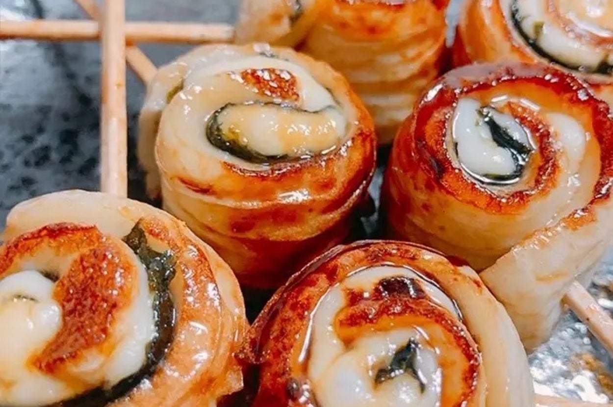 焼き竹輪の串刺しが黒い皿に盛られている。具材が巻かれて焼かれている様子が見える。