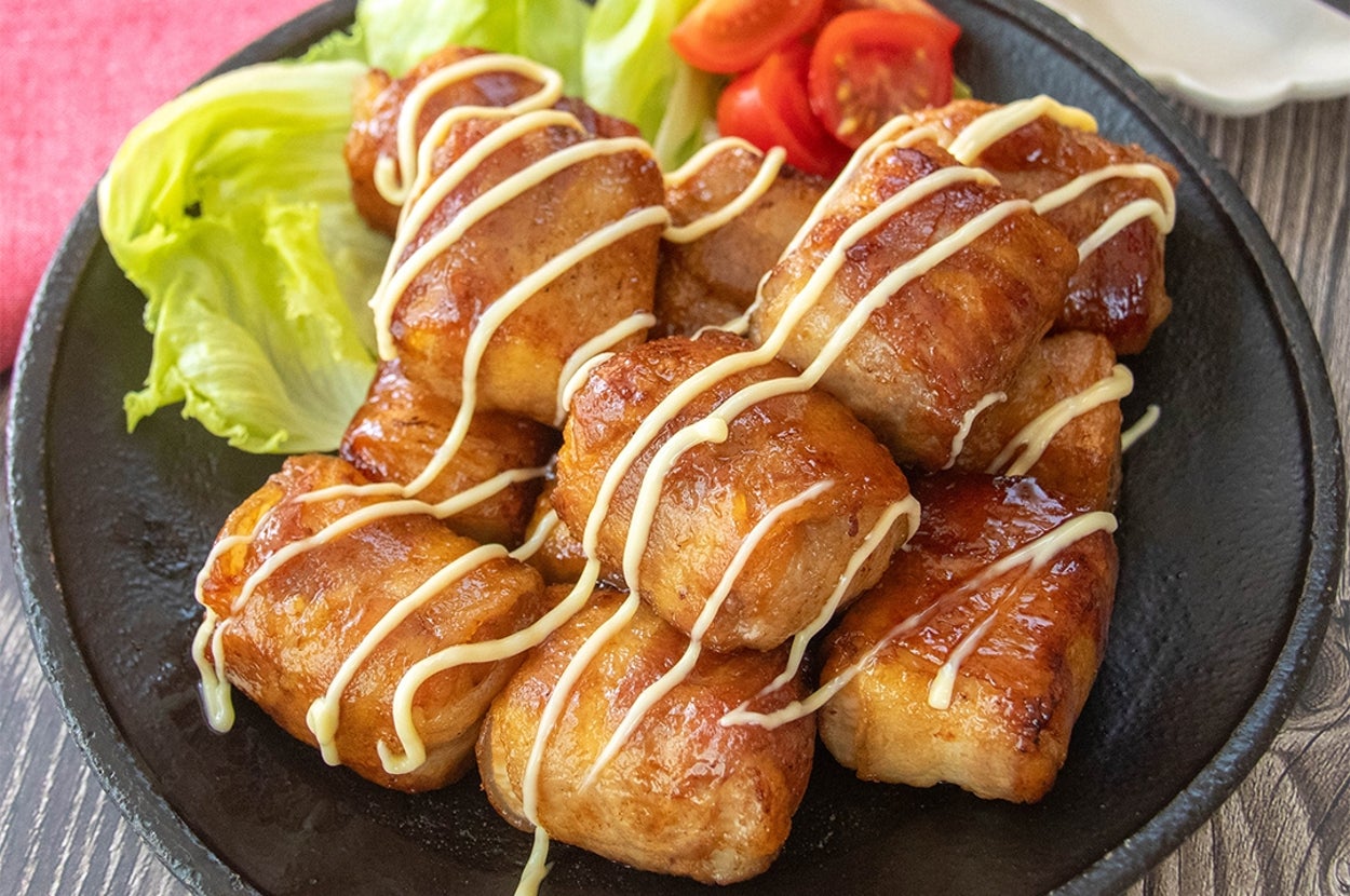 黒い皿に乗った焼いた厚揚げの肉巻きにマヨネーズがかかっており、レタスとトマトが添えられています。