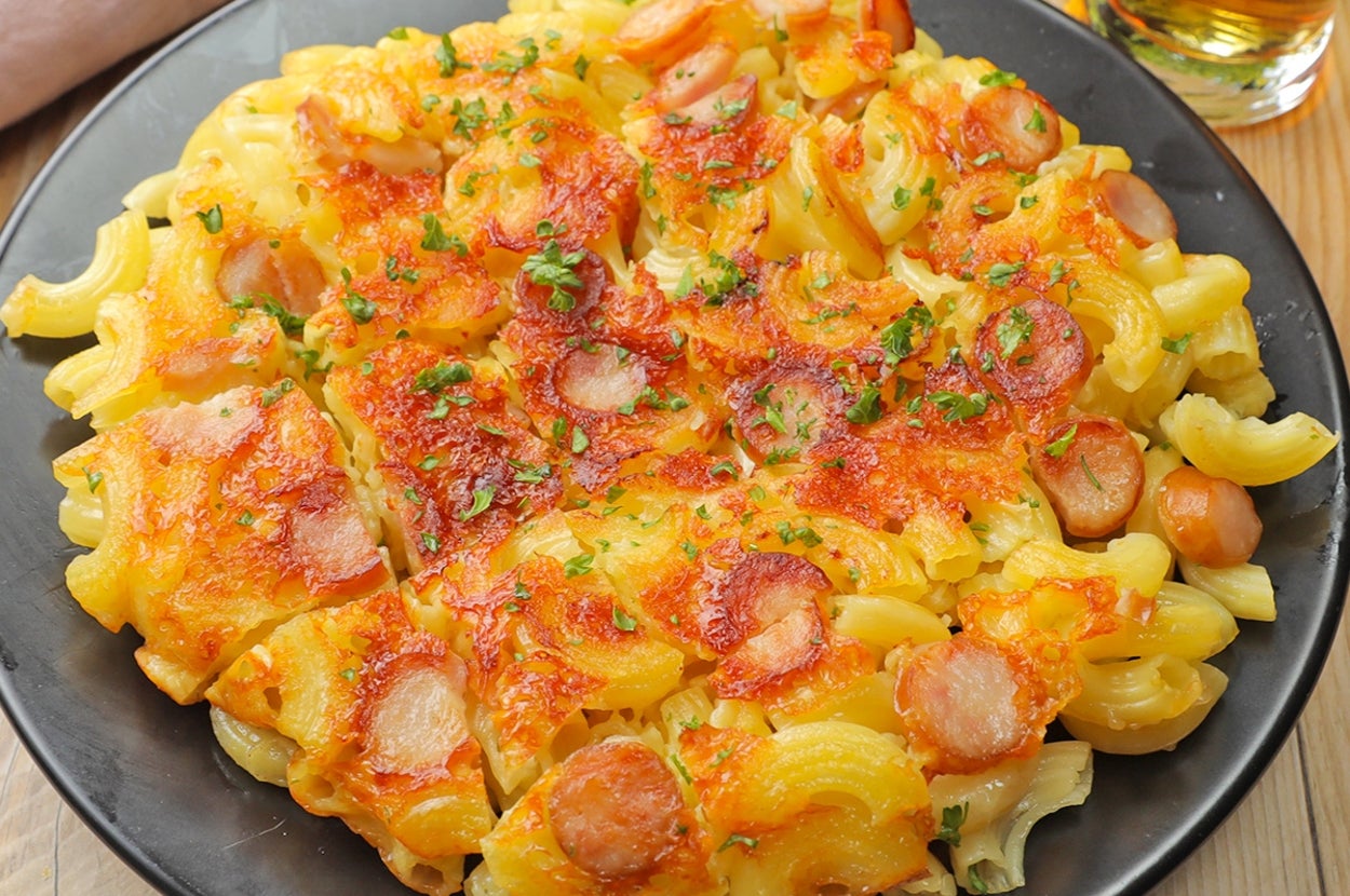 マカロニとソーセージの焼きパスタ、上に溶けたチーズとパセリがトッピングされた料理が黒い皿に盛られています。