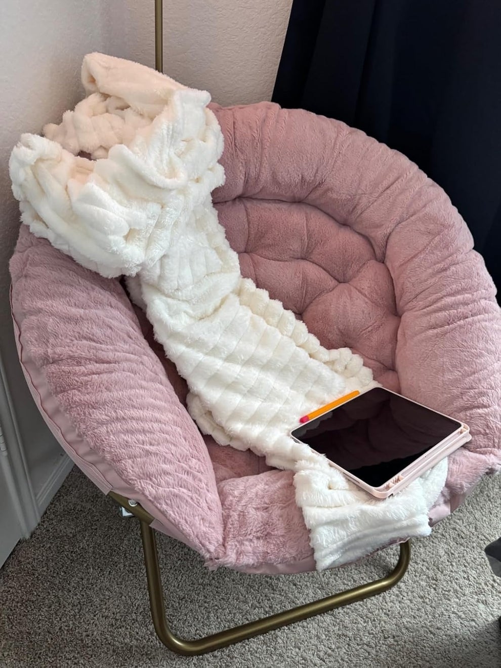 Cozy pink chair with a fluffy white blanket and a tablet resting on top, suitable for a comfortable reading or browsing experience