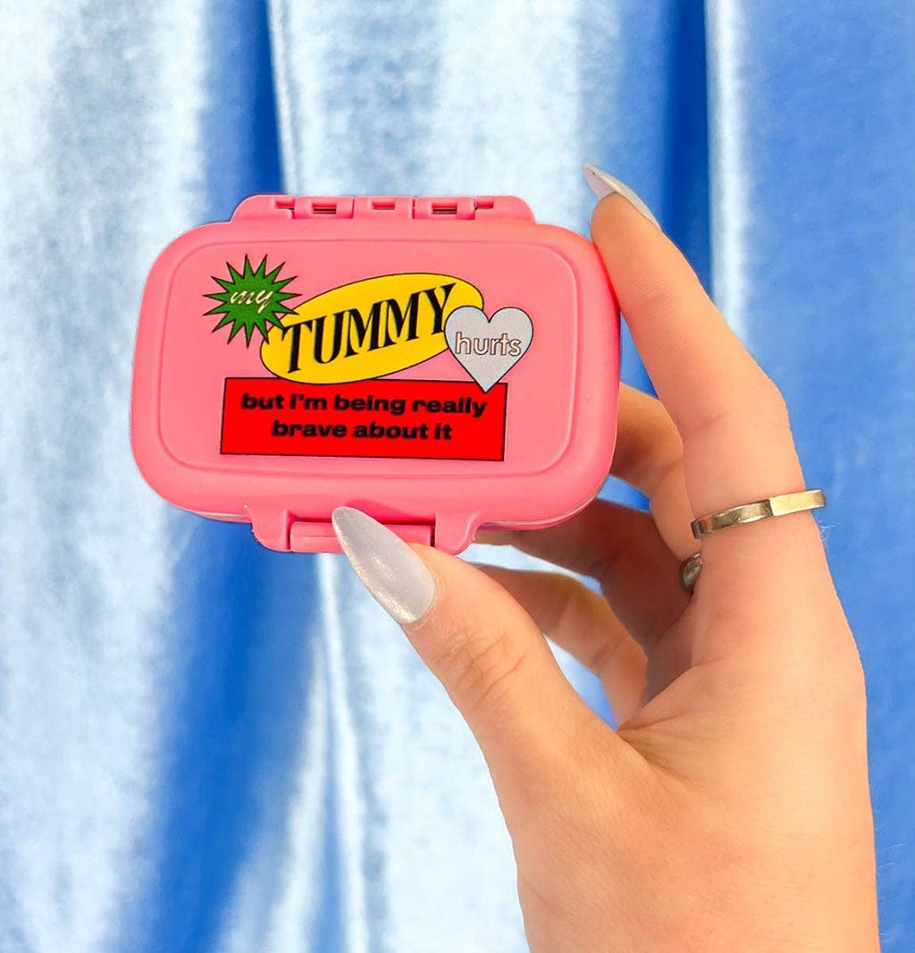 hand holding pink pill box that reads "my tummy hurts but I'm being really brave about it"