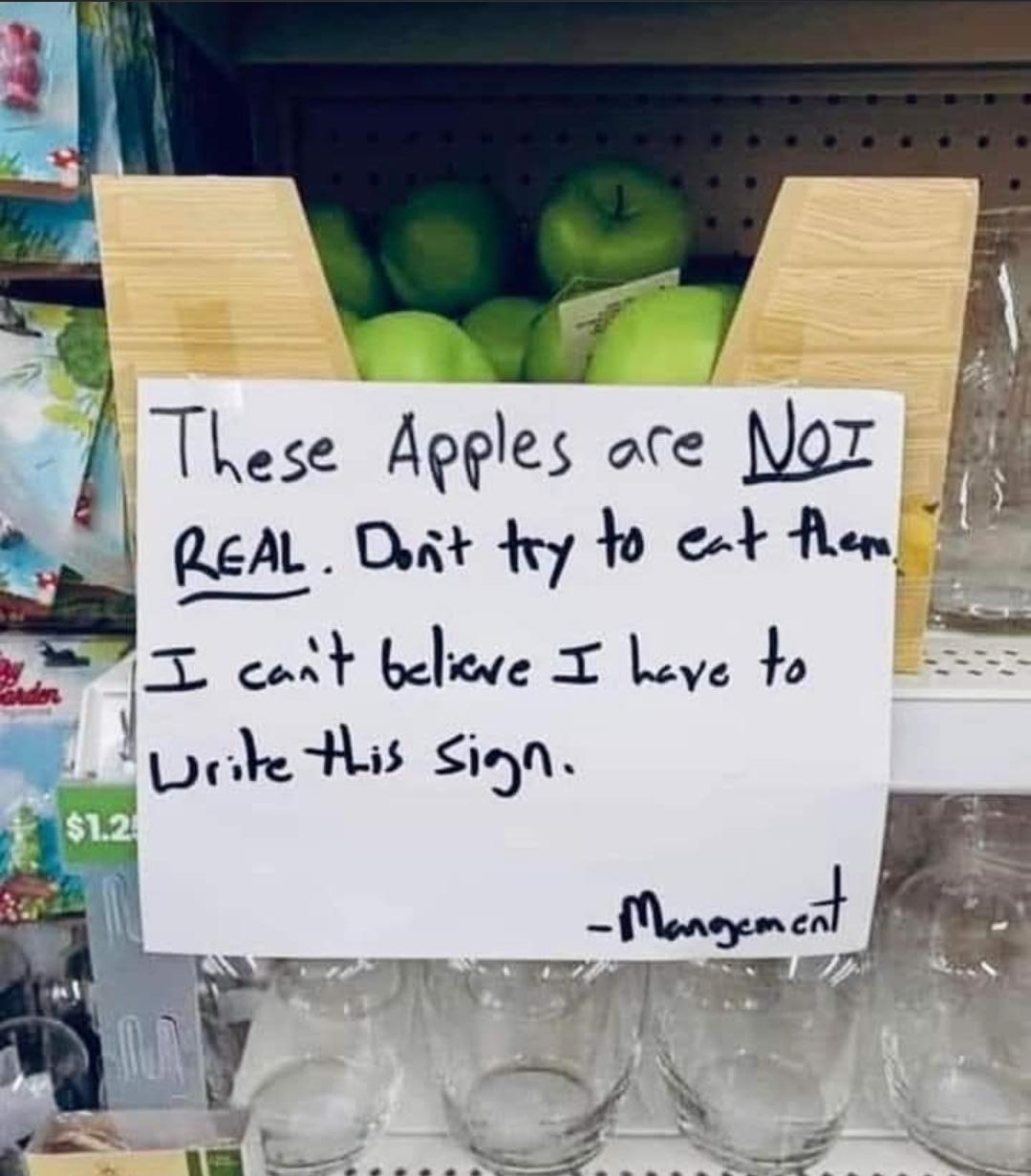 Sign on a shelf of decorative apples: "These apples are NOT real. Don't try to eat them. I can't believe I have to write this sign. -Management"