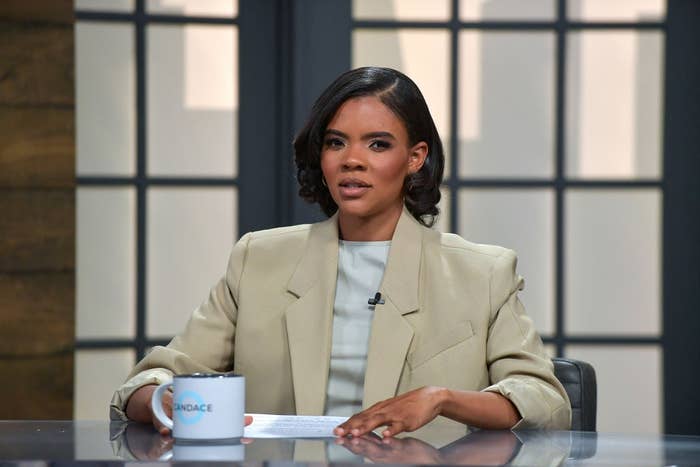 Candace Owens on the set of &quot;Candace&quot; seated at a desk, holding a mug, wearing a tailored blazer over a light top