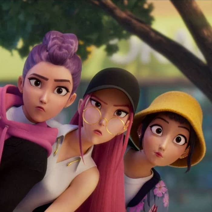 Tres personajes animados con expresiones sorprendidas; uno lleva bufanda rosa, otro con gorra y gafas, y el tercero un sombrero amarillo