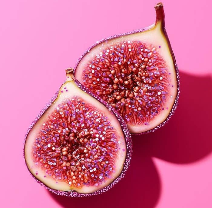 Two fig halves with glistening seeds lie on a pink surface, highlighting their texture and detail
