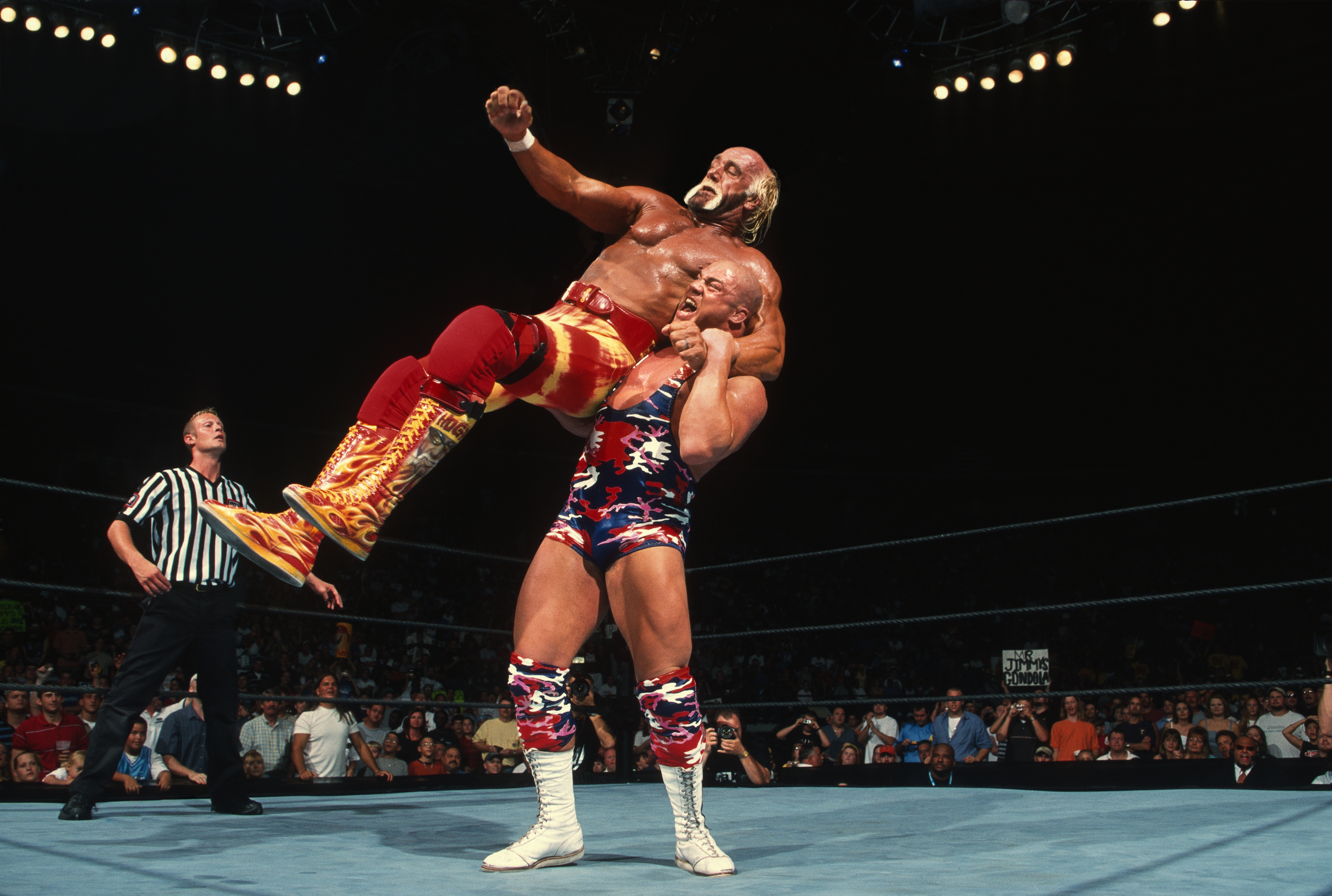 Kurt Angle lifts Hulk Hogan in a dramatic wrestling match, both wearing stylized gear