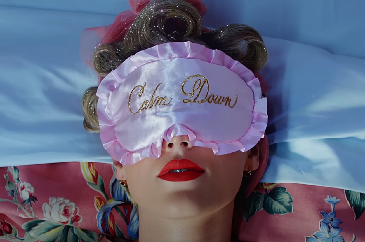 Taylor Swift in bed wearing an eye mask that says Calm Down in the You Need to Calm Down music video