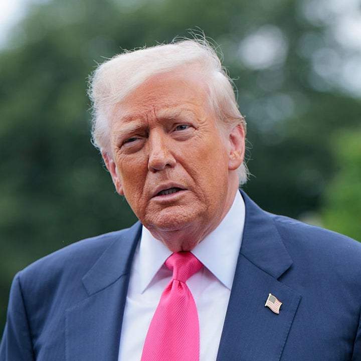 Man in a suit with a tie, standing outdoors with trees in the background