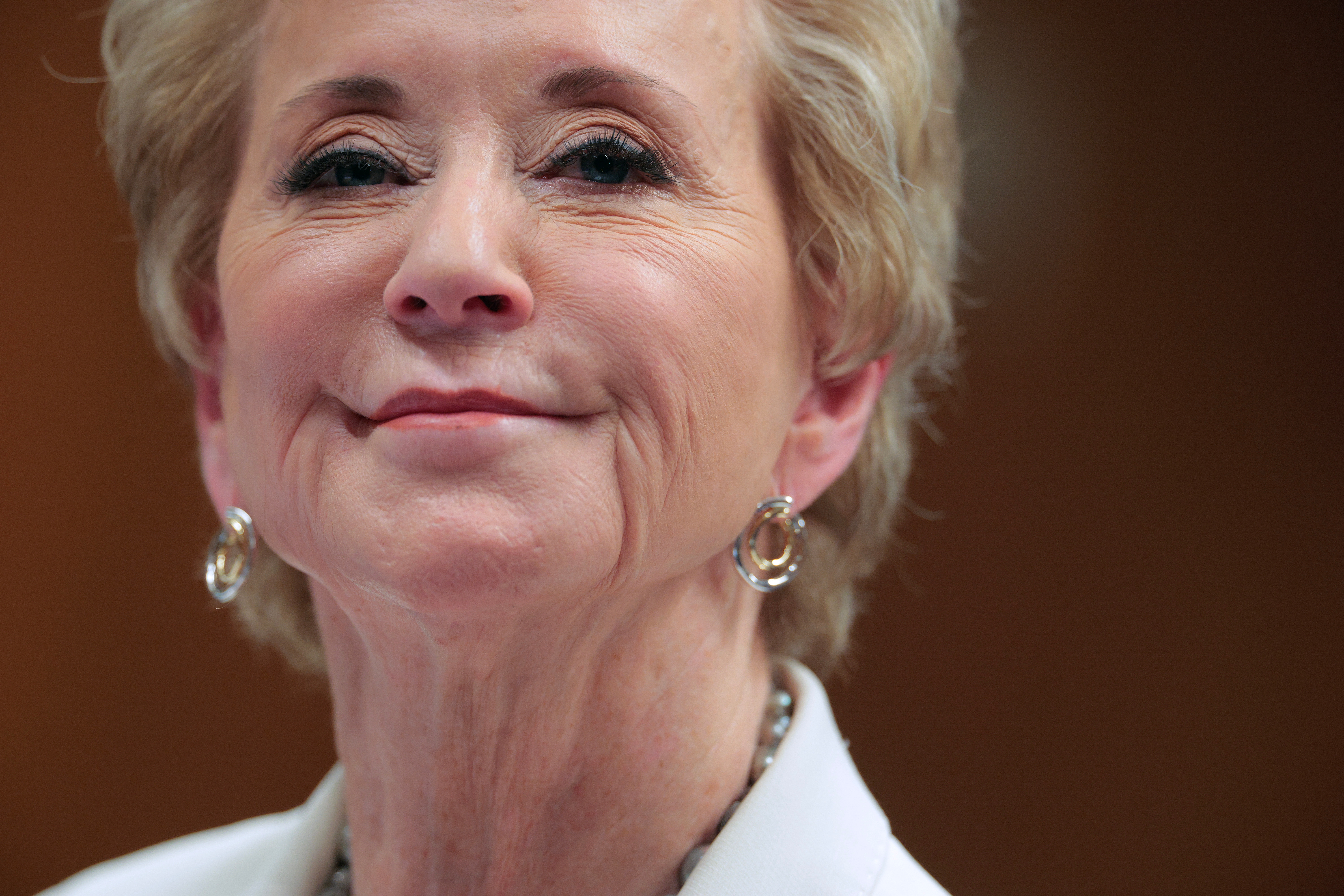 Linda McMahon with short hair smiles slightly, wearing hoop earrings and a blazer