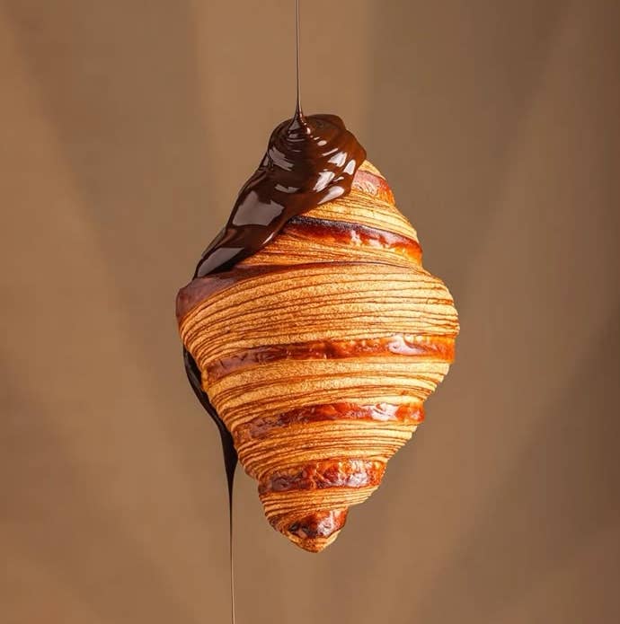 Croissant colgado con chocolate derramándose sobre él. Fondo liso sin detalles adicionales
